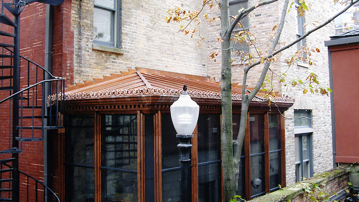 Straight eave, lean-to, complex hip end conservatory with eave cresting, copper standing seam roof, gutter, and downspouts, and decorative crown molding.