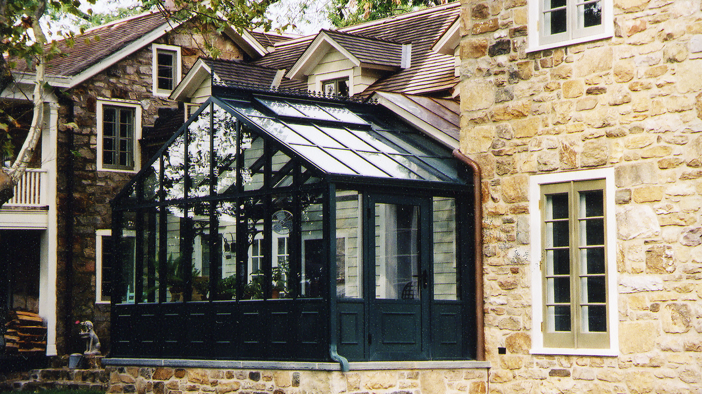 Straight eave double pitch, conservatory greenhouse with decorative base panels, ridge cresting, and operable ridge vents.