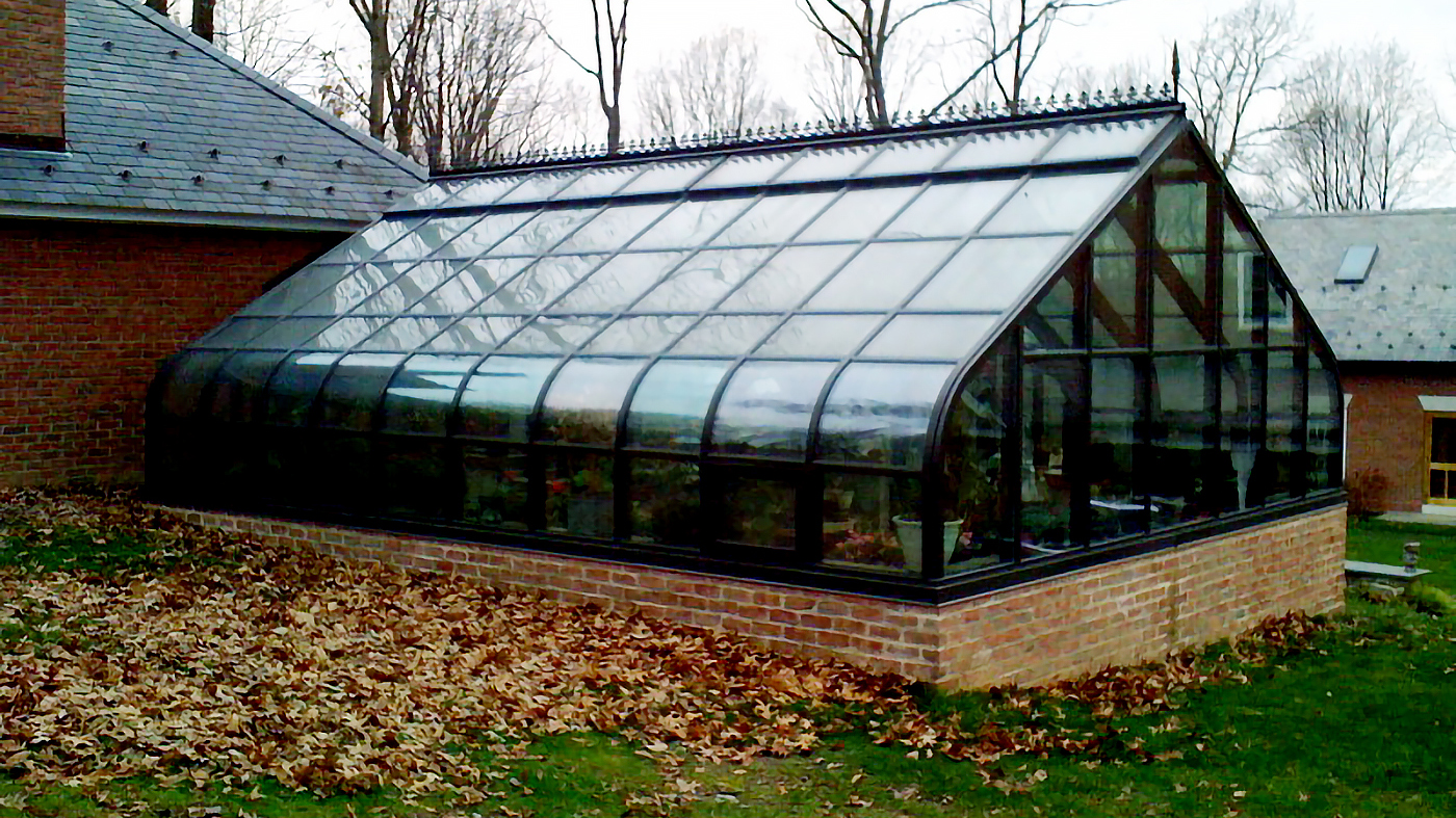 Curved eave double pitch greenhouse with two gable ends and a curved eave double pitch dormer with one gable end. Features operable ridge vent, decorative alumnim ridge cresting, terrace door and interior ring and collar.