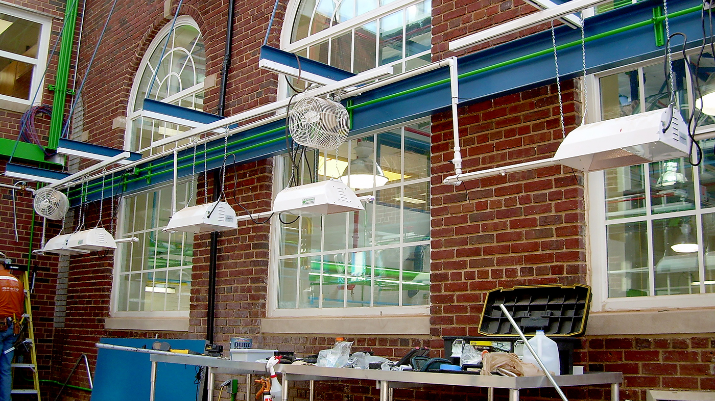 Straight eave double pitch educational greenhouse with only a front wall and sloped roof, constructed out of a vertical curtain wall using polycarbonate and skylight system. Interior accessories include shading, circulation fans, grow lights, misting system, benches, and control system.