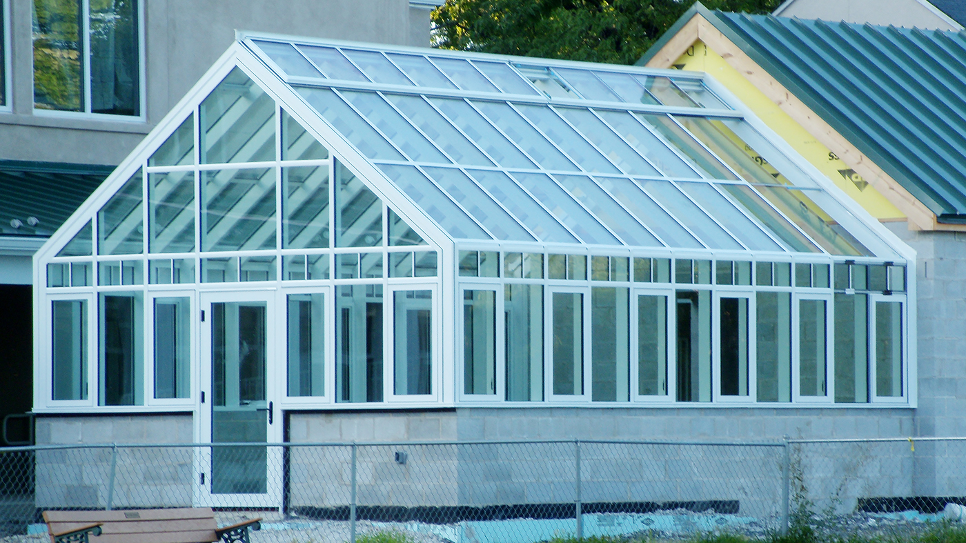 Straight eave double pitch greenhouse used at a retirement community. Unit includes ridge vents, transoms with grids, casement windows, terrace door, interior circulation fans, grow lights and interior roof mounted shades.