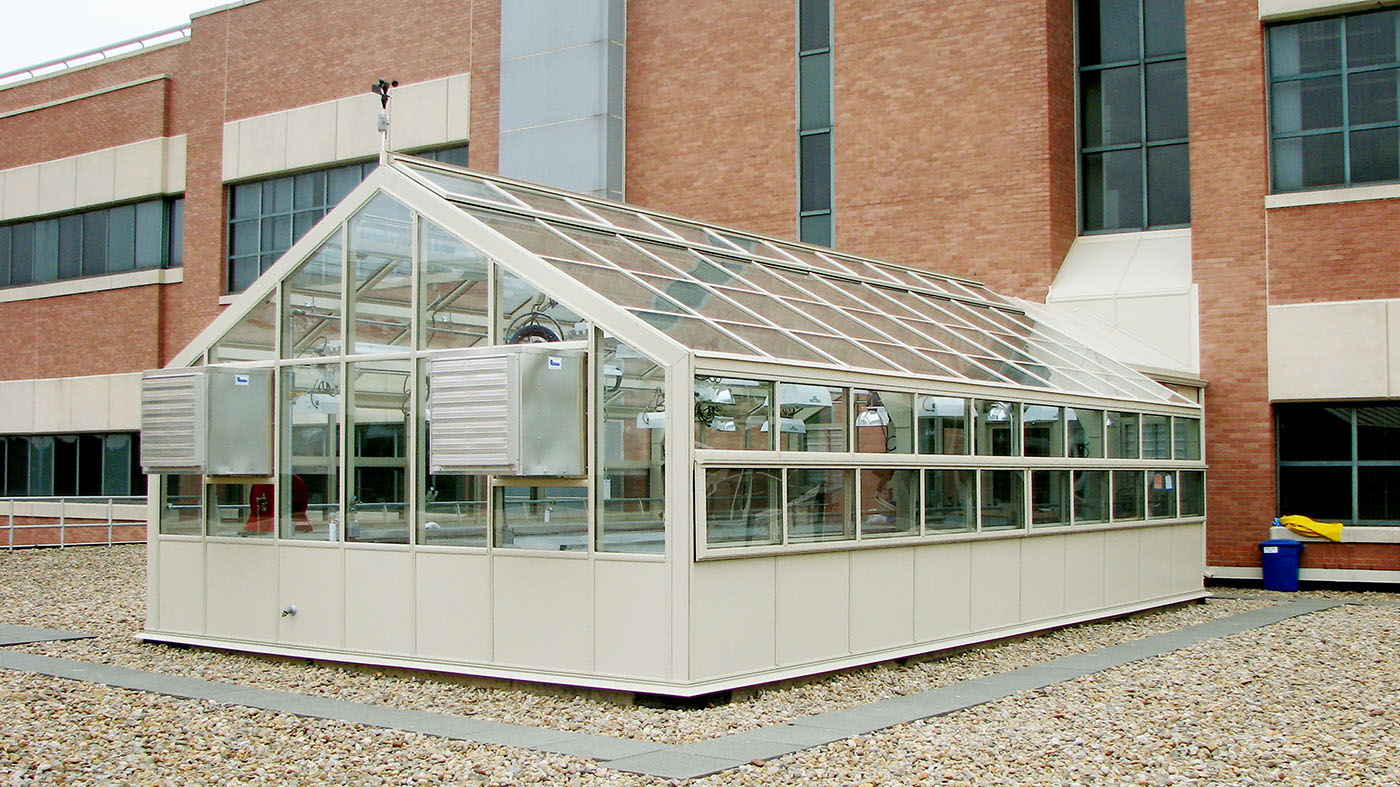 Straight eave, double pitch greenhouse with connecting walkway, ridge vents, eave vents, terrace door, environmental control system, benches, base panels, and gutter.
