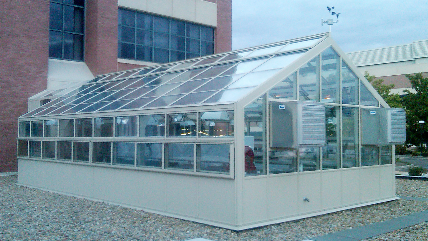 Straight eave, double pitch greenhouse with connecting walkway, ridge vents, eave vents, terrace door, environmental control system, benches, base panels, and gutter.