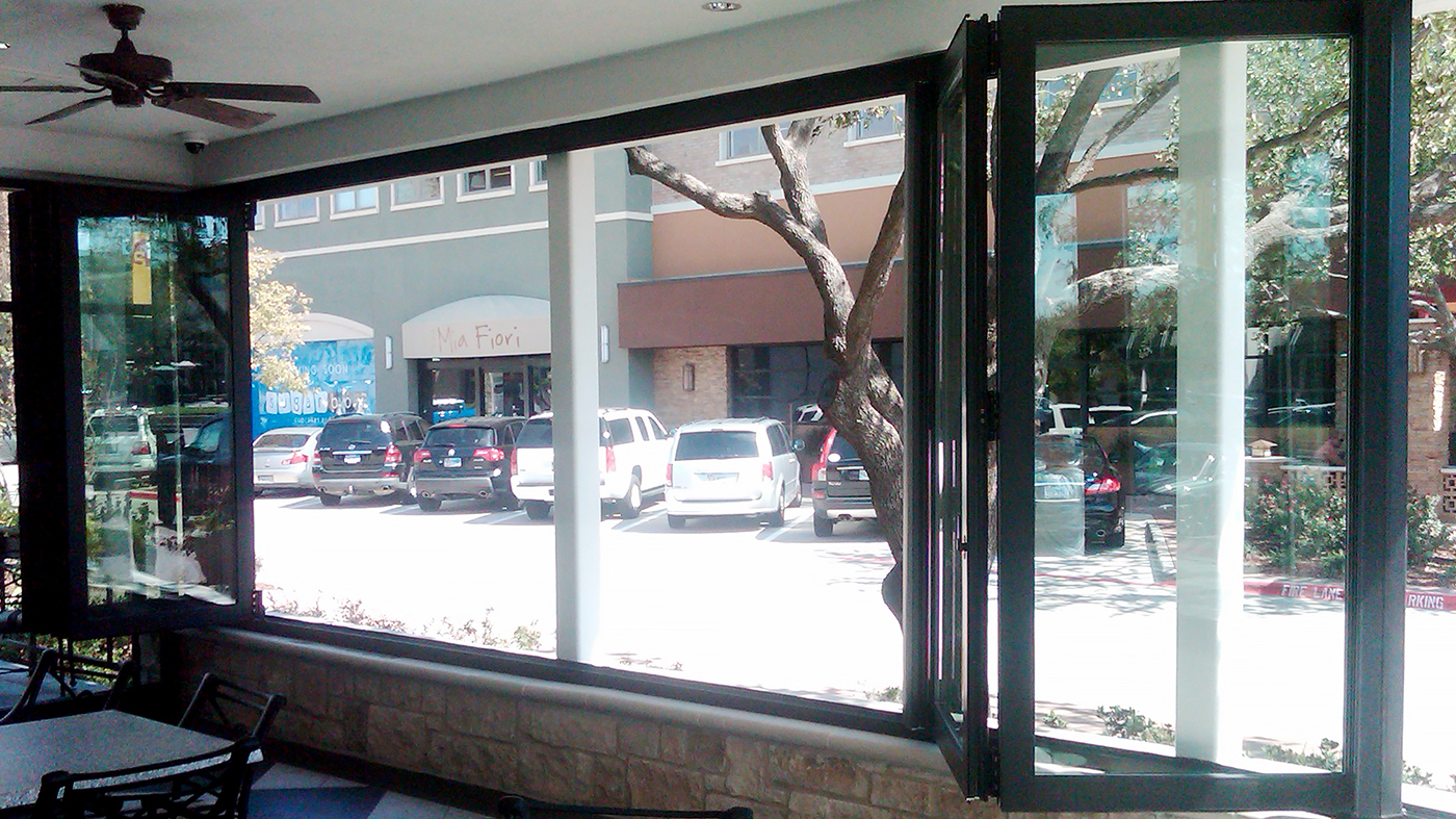 One segmented radius split folding glass wall with dual wheel trolley system - used in a restaurant setting.