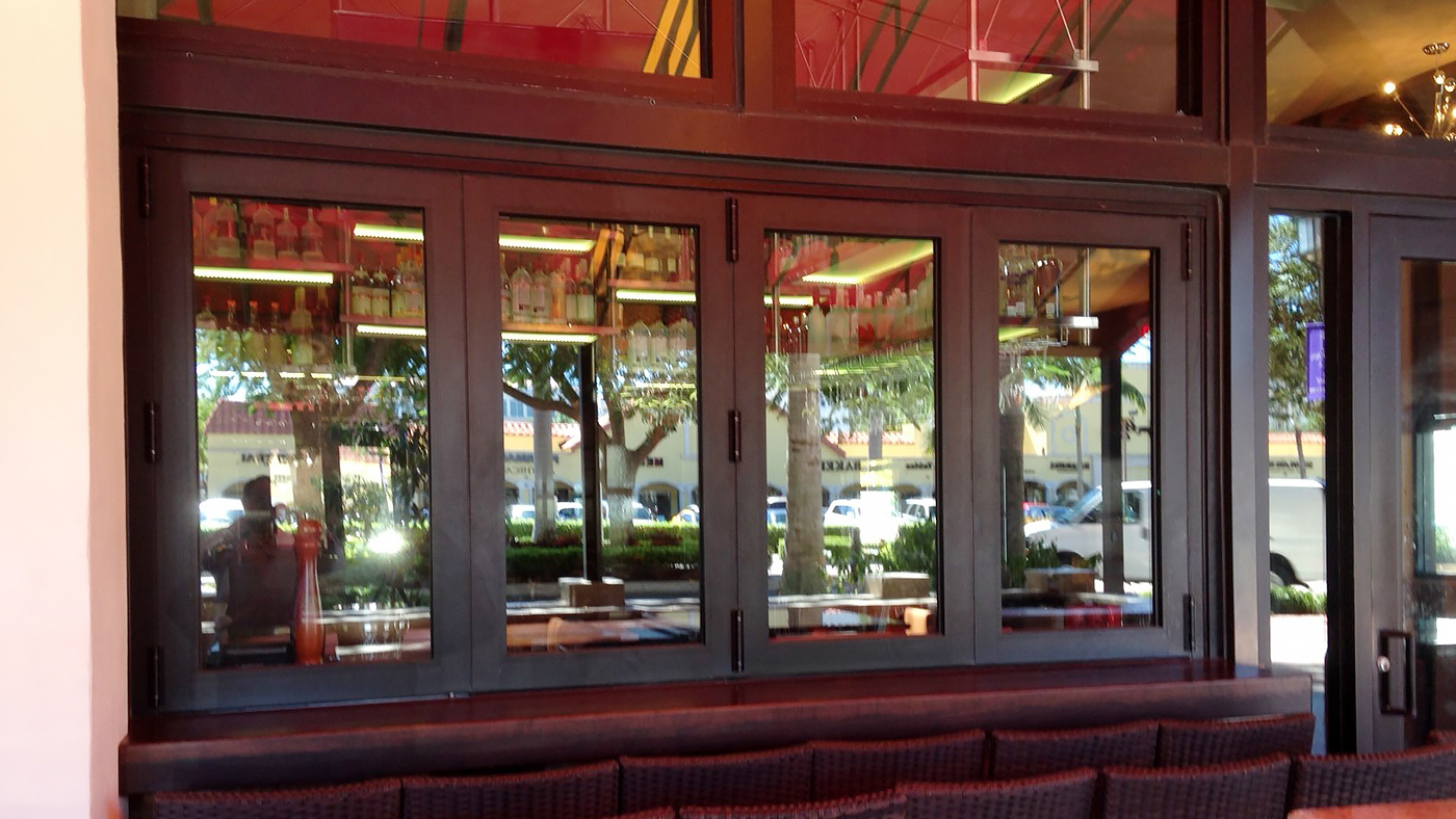 Multiple sets of folding glass windows and folding glass walls used at a restaurant with impact glazing. Each unit has an all wall configuration, folds out, and uses varying sills.