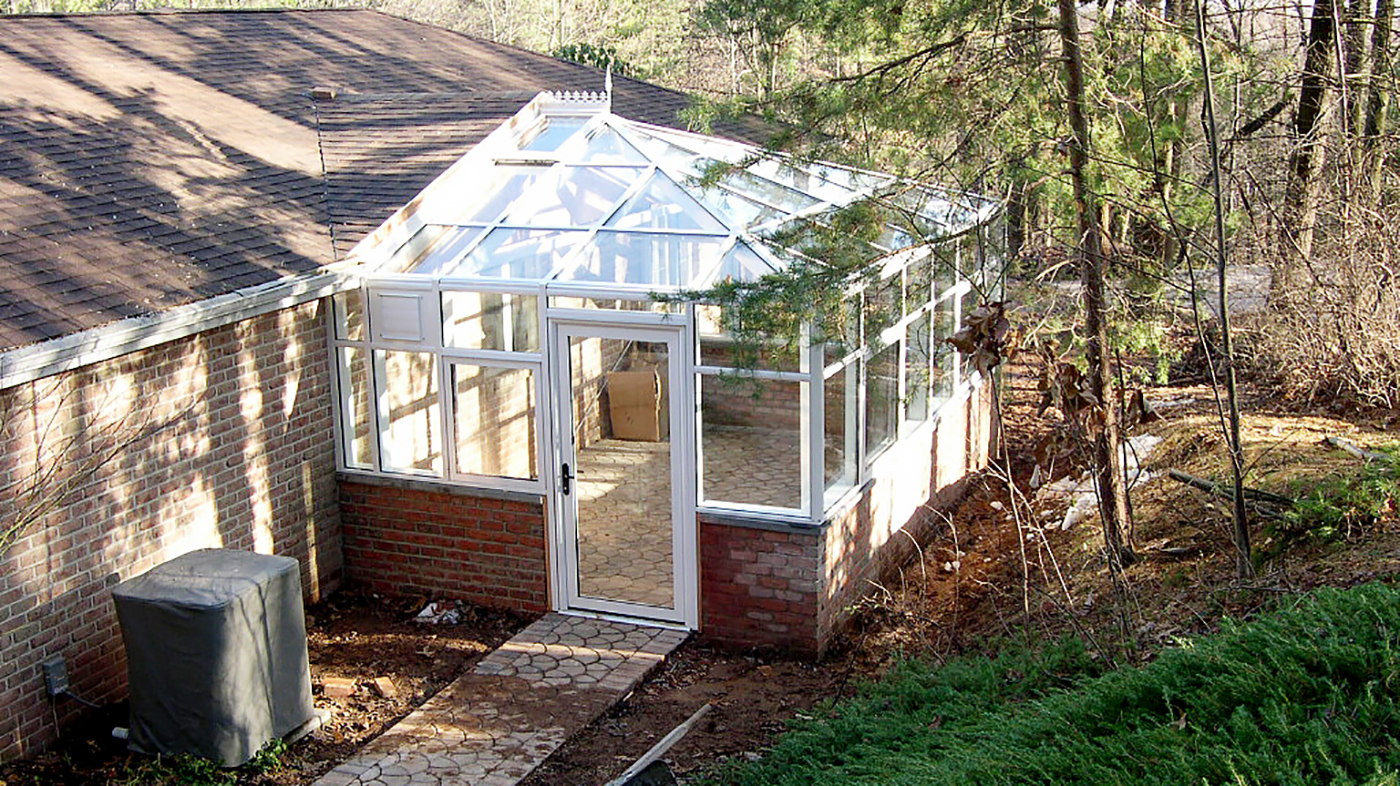 Straight eave, double pitch greenhouse with one hip end, awning windows, terrace door, ridge vents, finial, and ridge cresting.