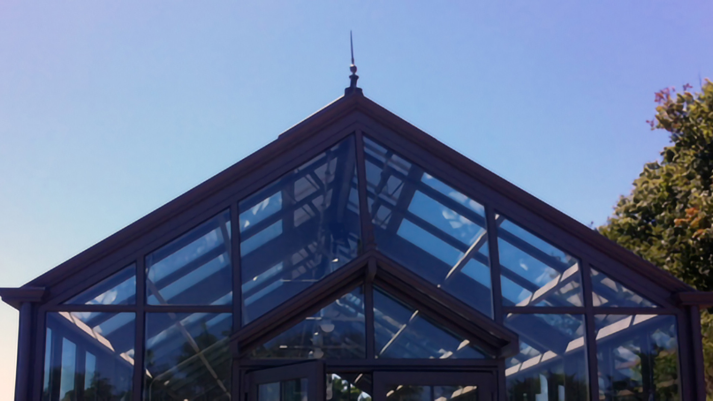 This straight eave, double pitch greenhouse with two gable ends includes two canopies and multiple accessories. Some of these accessories include aluminum base panels, bulbous trim, extruded gutter, round downspouts, ridge cresting, and multiple finials. The structure also features a custom 