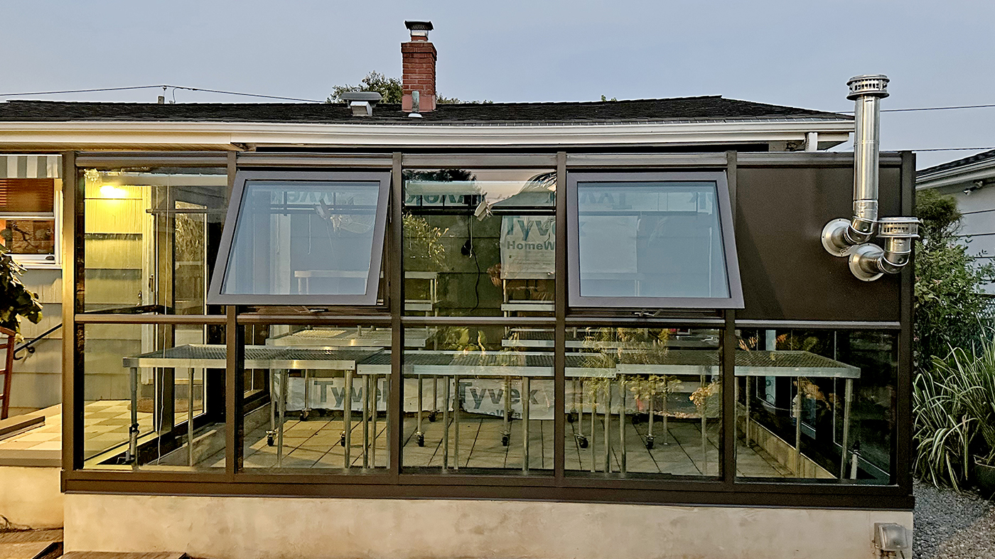 Straight eave lean-to greenhouse with three integrated awning windows and an outswing terrace door. The greenhouse has a one solid panel infill to allow for heater exhaust and a sink.