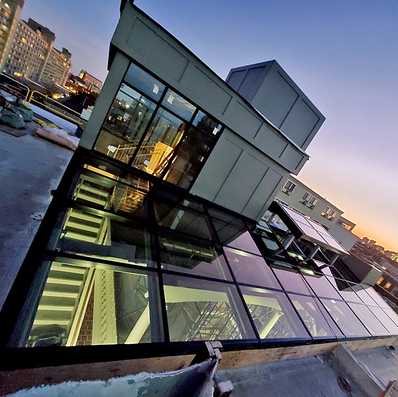 Irregular straight eave double pitch skylight with a cupola projection of the skylight protruding upward and supported on steel framing. The skylight covers a courtyard below.