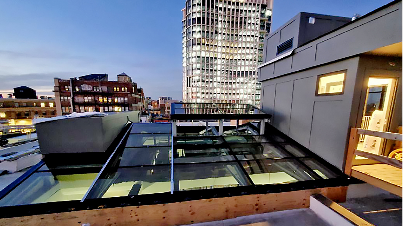 Irregular straight eave double pitch skylight with a cupola projection of the skylight protruding upward and supported on steel framing. The skylight covers a courtyard below.