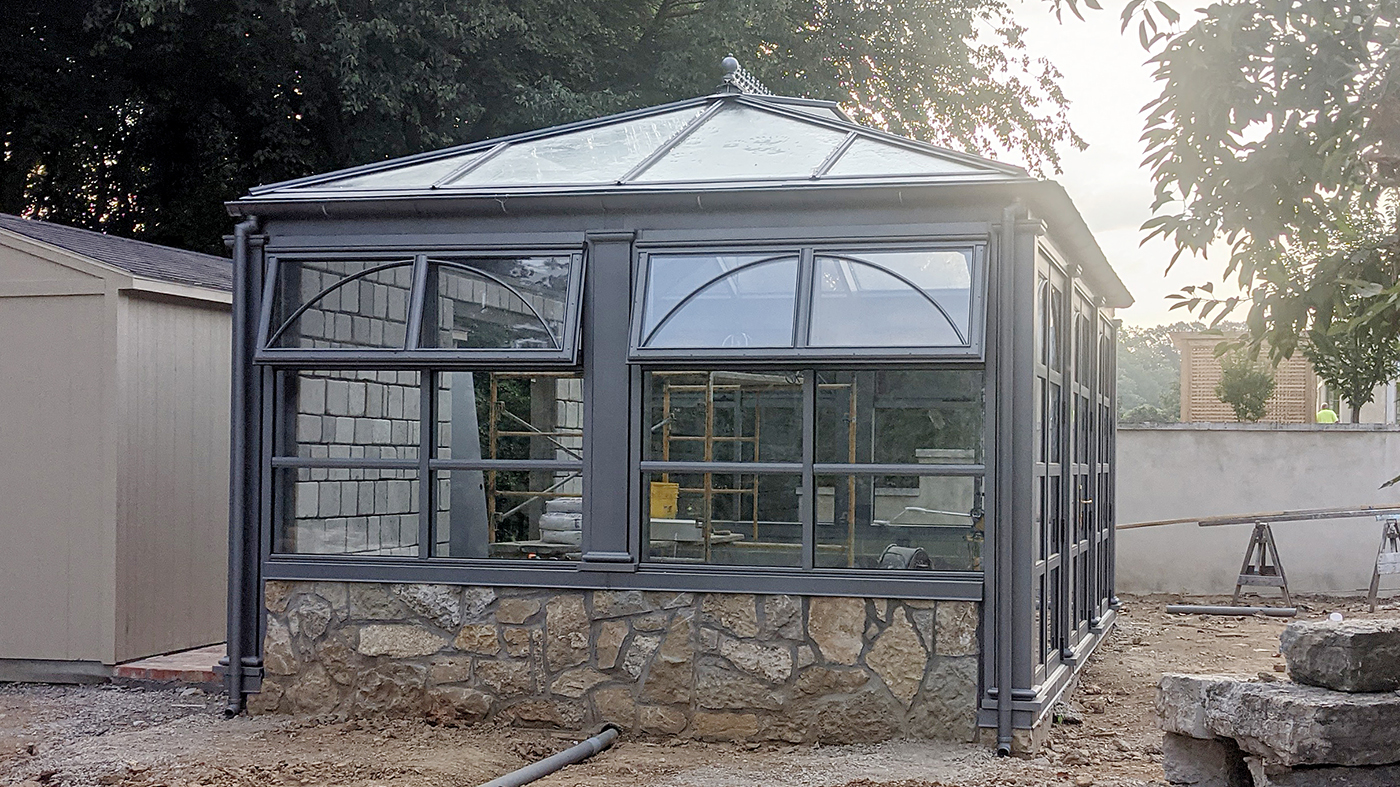 Straight eave double pitch hip end greenhouse with three sets of French doors with mullions and arched grids.