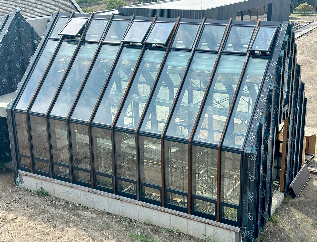Straight eave double pitch greenhouse built with existing exposed steel framing. There are 20 awning windows and 20 motorized ridge vents using WindowMaster actuators.