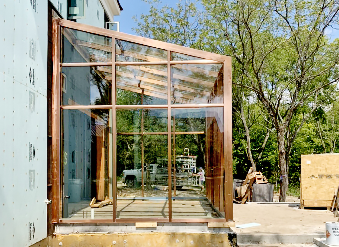 Straight eave lean-to greenhouse with copper cladding on the interior and exterior and cross bracing, with a single terrace door.