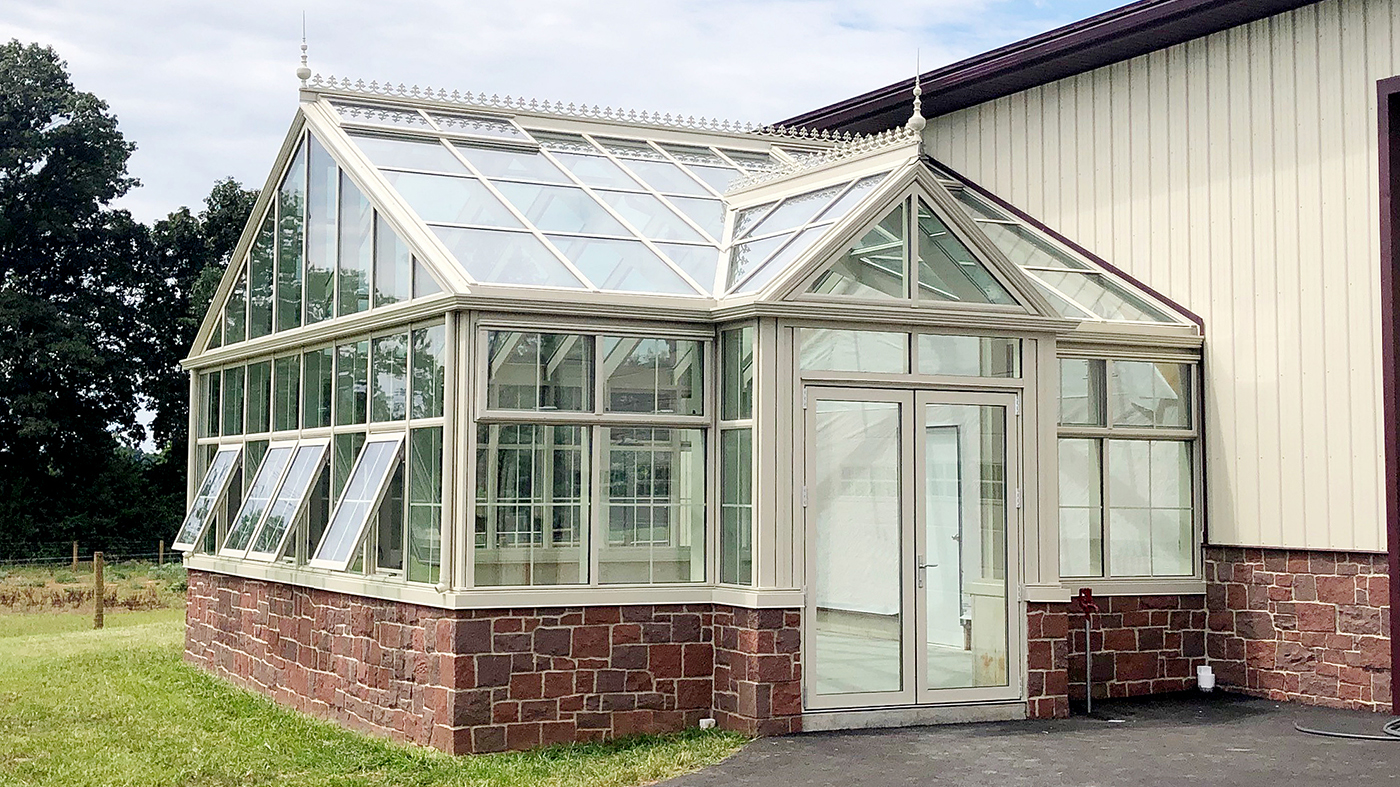 Straight eave double pitch greenhouse with a dormer, French doors, and four awning windows.