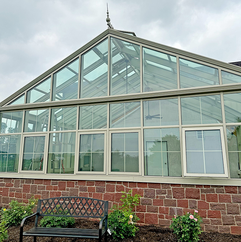 Straight eave double pitch greenhouse with a dormer, French doors, and four awning windows.
