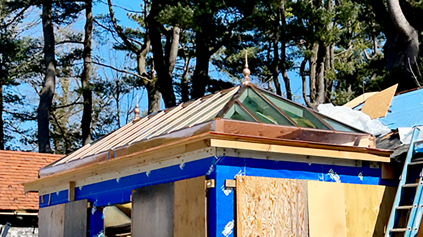 One straight eave double pitch skylight with two hip ends and a dormer that connects to building, clad in copper.