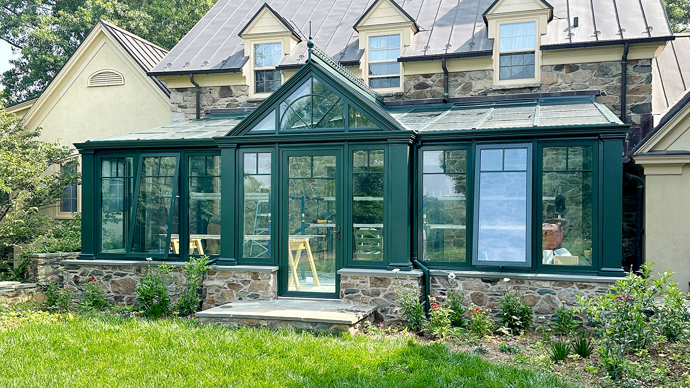 One straight eave lean-to conservatory with a dormer, two integrated inswing terrace doors, and four awning windows with a detail shot of how the structure butts against a stone wall.