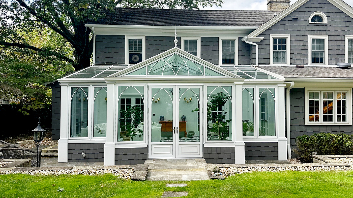 Straight eave lean-to conservatory adorned with Gothic Arch grids with two sets of French doors, awning windows, and a dormer.